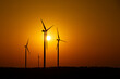 Silhouettes of wind turbines against the setting sun