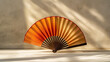 An ornate fan with a warm spectrum of colors casts a delicate shadow on a sunlit neutral wall.