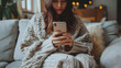 Happy millennial hispanic teen girl checking social media holding smartphone at home. Smiling young latin woman using mobile phone app playing game, shopping online, ordering delivery relax on sofa.