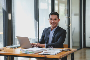 Wall Mural - Smiling businessman using laptop at office desk. Professional workplace and success concept.