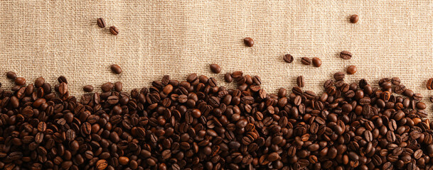  Many coffee beans on burlap fabric, top view. Space for text