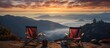 Two chairs are placed on the top of a mountain peak, offering a breathtaking view of the surrounding mountains and landscape