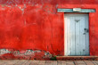 a red wall with a white door and a brick sidewalk in front of it and a brick sidewalk in front of the door and a red wall with a white door.