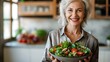Ältere Frau lächelt glücklich und hält eine gesunde Schüssel voll Salat, blurred Küche im Hintergrund, Konzept gesunde Ernährung im Alter