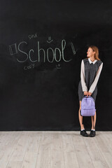 Wall Mural - Female student with backpack standing near word SCHOOL written on blackboard. End of school concept