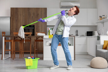 Wall Mural - Young man having fun with floor mop in kitchen