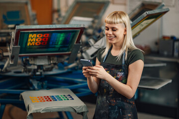 Female print shop worker taking orders on phone app at facility.