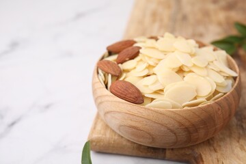 Fresh almond flakes and nuts in bowl on white table, closeup. Space for text