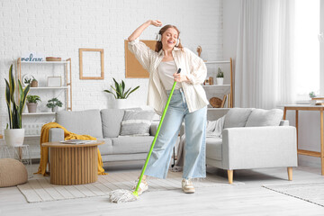 Wall Mural - Happy young woman in headphones with mop dancing at home