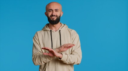 Wall Mural - Arab male model doing no symbol on blue backdrop, showing his rejection and denial in studio. Middle eastern guy expressing refusal with a negative gesture, serious man. Camera 1.