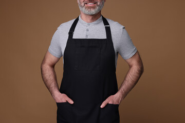 Poster - Man wearing kitchen apron on brown background, closeup. Mockup for design