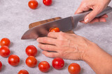 Fototapeta Na ścianę - The housewife slicing fresh tomatoes with a large kitchen knife on a wooden chopping board, closeup with selective focus