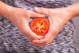 Fototapeta Na ścianę - Sliced tomato in hands. Woman holding half a tomato, closeup with selective focus