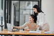 © Satori Studio - Two smiling female colleagues collaboratively working on a project with a laptop and coffee in a bright office space.