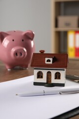 Wall Mural - House model, piggy bank, clipboard and pen on wooden table indoors, selective focus