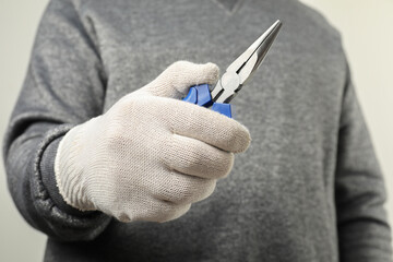 Canvas Print - Man with needle nose pliers on light background, closeup. Space for text