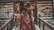 A cowgirl in a fringed leather jacket strides across the wooden planks cowboy hat pulled down low hiding face from view. . .
