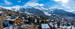 Panoramic aerial view of Verbier, Switzerland, displays chalets in a valley against snow capped mountains, merging natural beauty with alpine architecture under a clear sky.