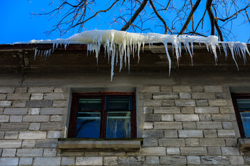 Wall Mural - Large icicles on the roof pose a danger to passersby. Background with selective focus and copy space