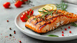 A piece of salmon is on a white plate with lemon slices and herbs. The salmon is grilled and looks delicious