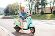 Young beautiful smiling hipster female in trendy clothes. Carefree woman driving retro motorbike on the street background. Positive model having fun, riding classic Italian scooter in Europe city