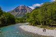 Hikers on the bank of a clear river leading towards snow-capped mountains (Japanese Alps, Nagano)