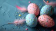   Three Easter eggs, two pink and one blue, sit on a blue surface Confetti sprinkles cover the area around them, and a pink feather rests beside the blue egg