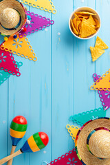 Wall Mural - Vibrant Cinco de Mayo top view vertical display with sombreros and maracas. Bright flag garland, and spicy nacho on a blue wooden desk. Space available for text