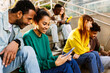 © Xavier Lorenzo - Group of young people using mobile phone sitting at staircase in the city. Millennial student friends having fun watching social media content on cell app. Technology lifestyle concept