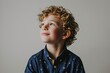 Portrait of a little curly boy in a blue shirt on a gray background