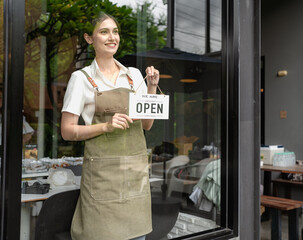 Smiling cafe owner, waitress woman showing open sign to welcome her coffee shop small business. Happy startup entrepreneur businesswoman standing at store window handing open sign ready to service