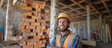 Fototapeta  - This portrait shows a happy bricklayer at a construction site. Content bricklayer donning a safety jacket and helmet.