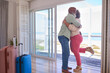 Loving Mature Couple With Luggage Arriving In Beachfront House Overlooking Ocean For Summer Vacation