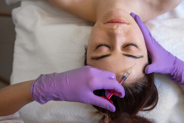 Wall Mural - Beautiful woman receiving beauty injections in forehead with closed eyes. Beautician doctor hands doing beauty procedure to female face with syringe