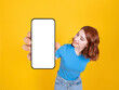 Digital mobile application offer, young caucasian red hair woman showing looking empty blank white screen phone mock up close up to camera. Yellow studio background. Advertisement concept idea image.
