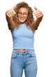 Beautiful caucasian teenager girl wearing casual clothes and glasses approving doing positive gesture with hand, thumbs up smiling and happy for success. winner gesture.