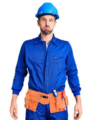 Canvas Print - Young handsome man wearing worker uniform and hardhat puffing cheeks with funny face. mouth inflated with air, crazy expression.