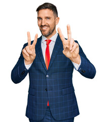 Wall Mural - Handsome man with beard wearing business suit and tie smiling looking to the camera showing fingers doing victory sign. number two.