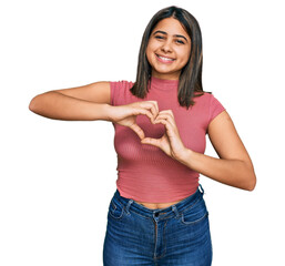 Canvas Print - Young hispanic girl wearing casual t shirt smiling in love doing heart symbol shape with hands. romantic concept.