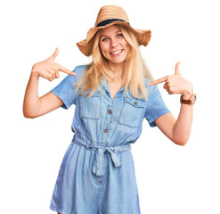 Wall Mural - Young beautiful blonde woman wearing summer hat and dress looking confident with smile on face, pointing oneself with fingers proud and happy.