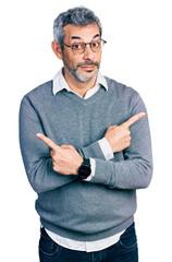 Wall Mural - Middle age hispanic with grey hair wearing glasses pointing to both sides with fingers, different direction disagree