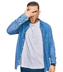 Wall Mural - Young caucasian man wearing casual clothes peeking in shock covering face and eyes with hand, looking through fingers with embarrassed expression.