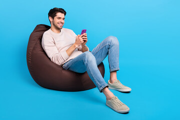 Poster - Full body portrait of nice young man sit bag use smart phone wear beige sweatshirt isolated on blue color background
