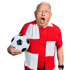 Canvas Print - Senior man with grey hair football hooligan holding ball angry and mad screaming frustrated and furious, shouting with anger. rage and aggressive concept.