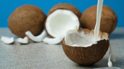 Wall Mural - Healthy vegan coconut milk pouring into half a coconut shell, splash of milk slow motion