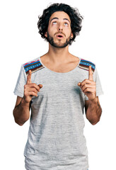 Poster - Young hispanic man wearing casual t shirt amazed and surprised looking up and pointing with fingers and raised arms.