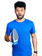 © Krakenimages.com - Young arab man with beard holding electric steam iron scared and amazed with open mouth for surprise, disbelief face