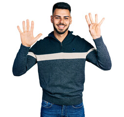 Wall Mural - Young hispanic man with beard wearing casual winter sweater showing and pointing up with fingers number nine while smiling confident and happy.