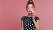 Portrait of a beautiful young pin up girl wearing polka dot dress standing isolated pink color background, showing macaroons professional photography.