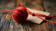 Close-up of a red yarn ball with a craft tag on a rustic wooden surface, conveying a cozy, handmade concept.